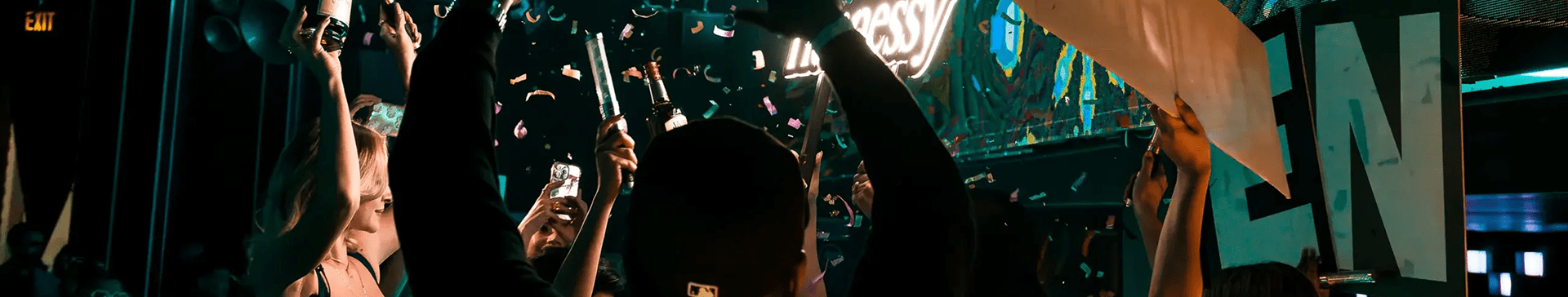 Guests celebrating in a nightclub with confetti, sparklers, and champagne bottles raised toward a glowing Hennessy sign.