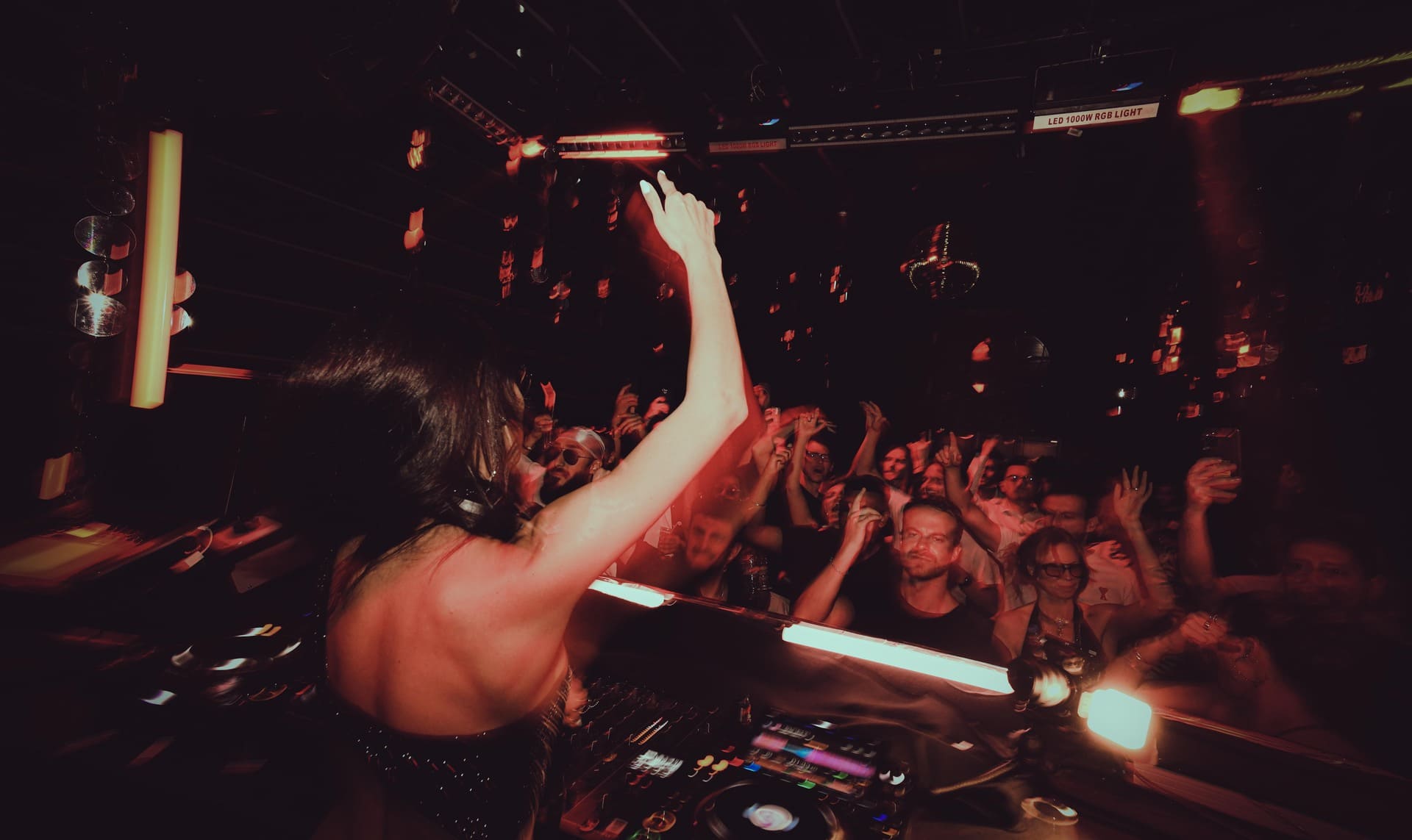 DJ performing on stage with crowd raising hands in a nightclub