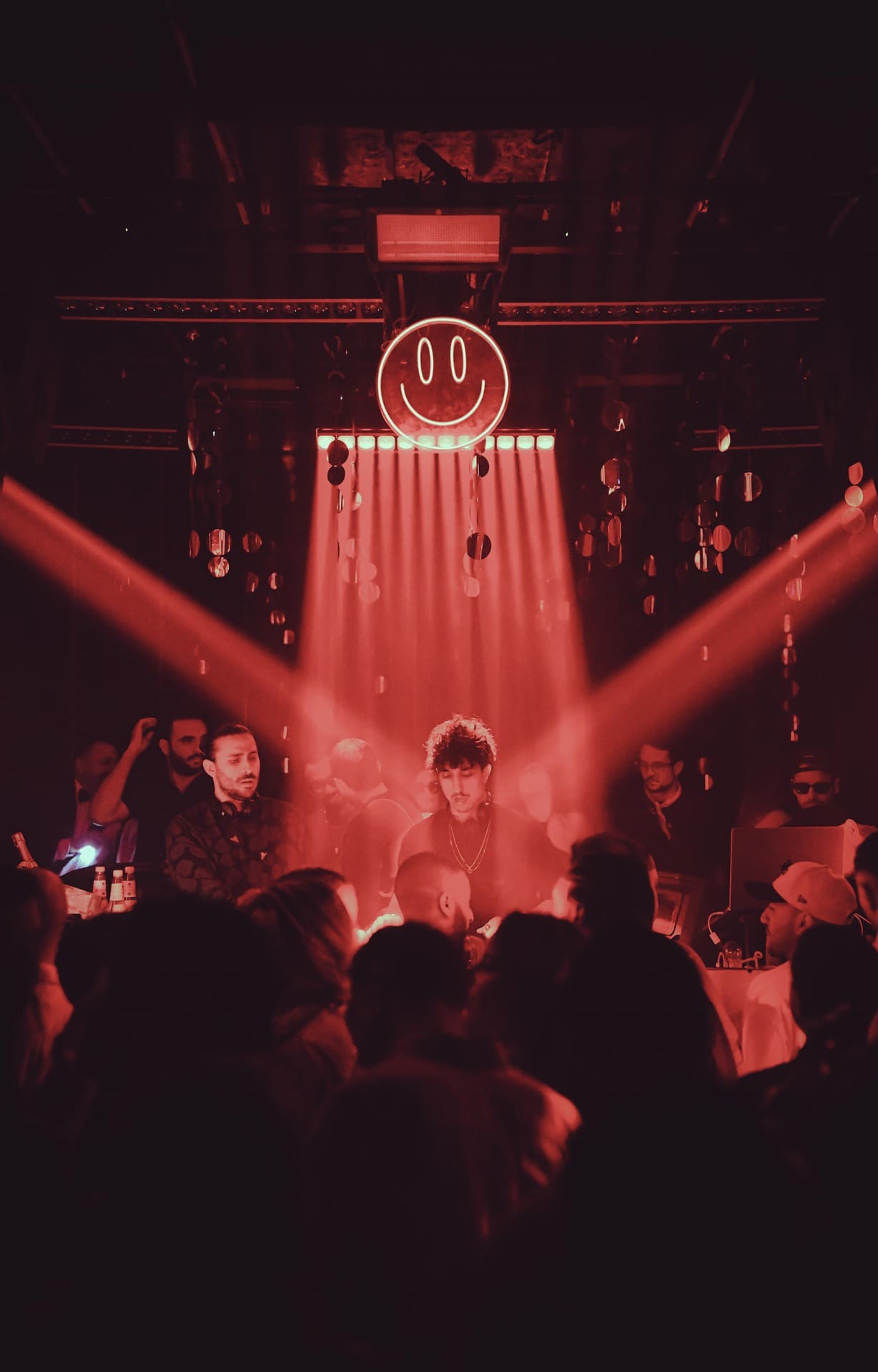 Crowded nightclub with DJ booth under red lighting and hanging decor