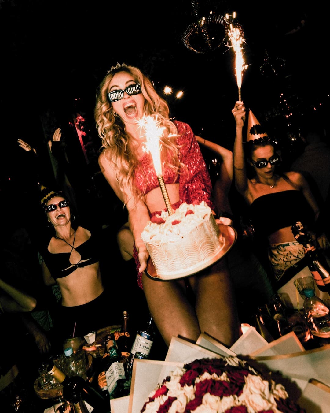 Person holding a birthday cake with sparklers during a lively celebration.