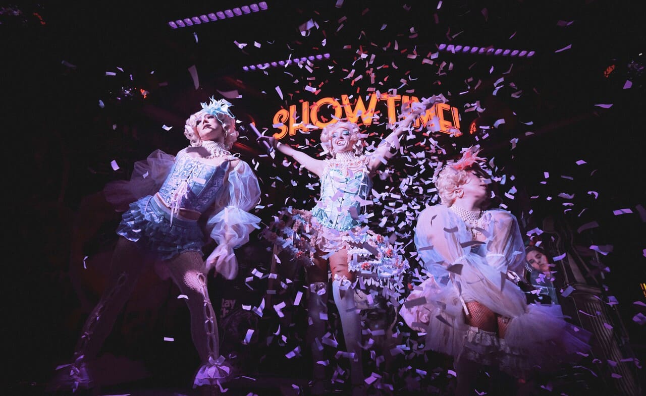 Costumed dancers celebrate on stage as confetti falls during a high-energy show.