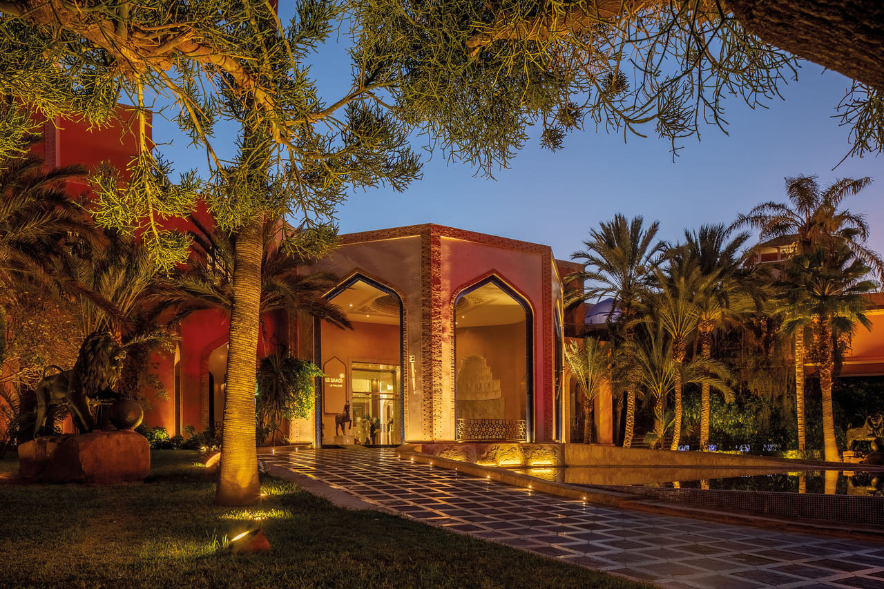 Illuminated main entrance of Es Saadi Marrakech Resort at night with palm trees