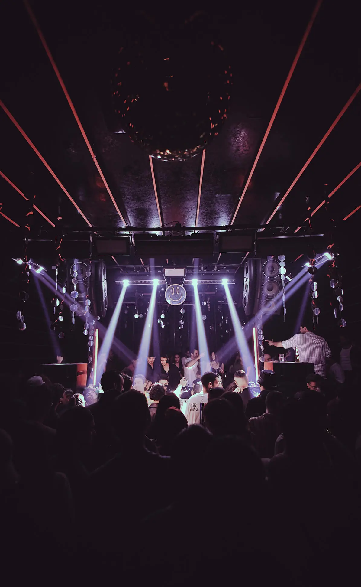 Crowd gathered on a nightclub dance floor under bright stage lights and disco ball.
